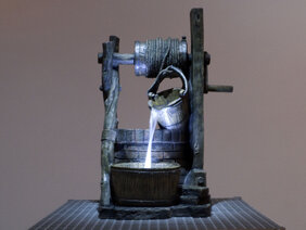 Ein Kunstwerk, das eine Art Brunnen abbildet. Aus dem hochgezogenen Eimer wird eine Flüssigkeit in das Brunnenbecken geschüttet