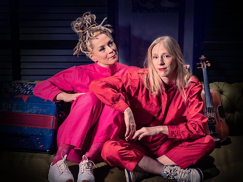 zwei blonde Frauen sitzend in pinken Overalls