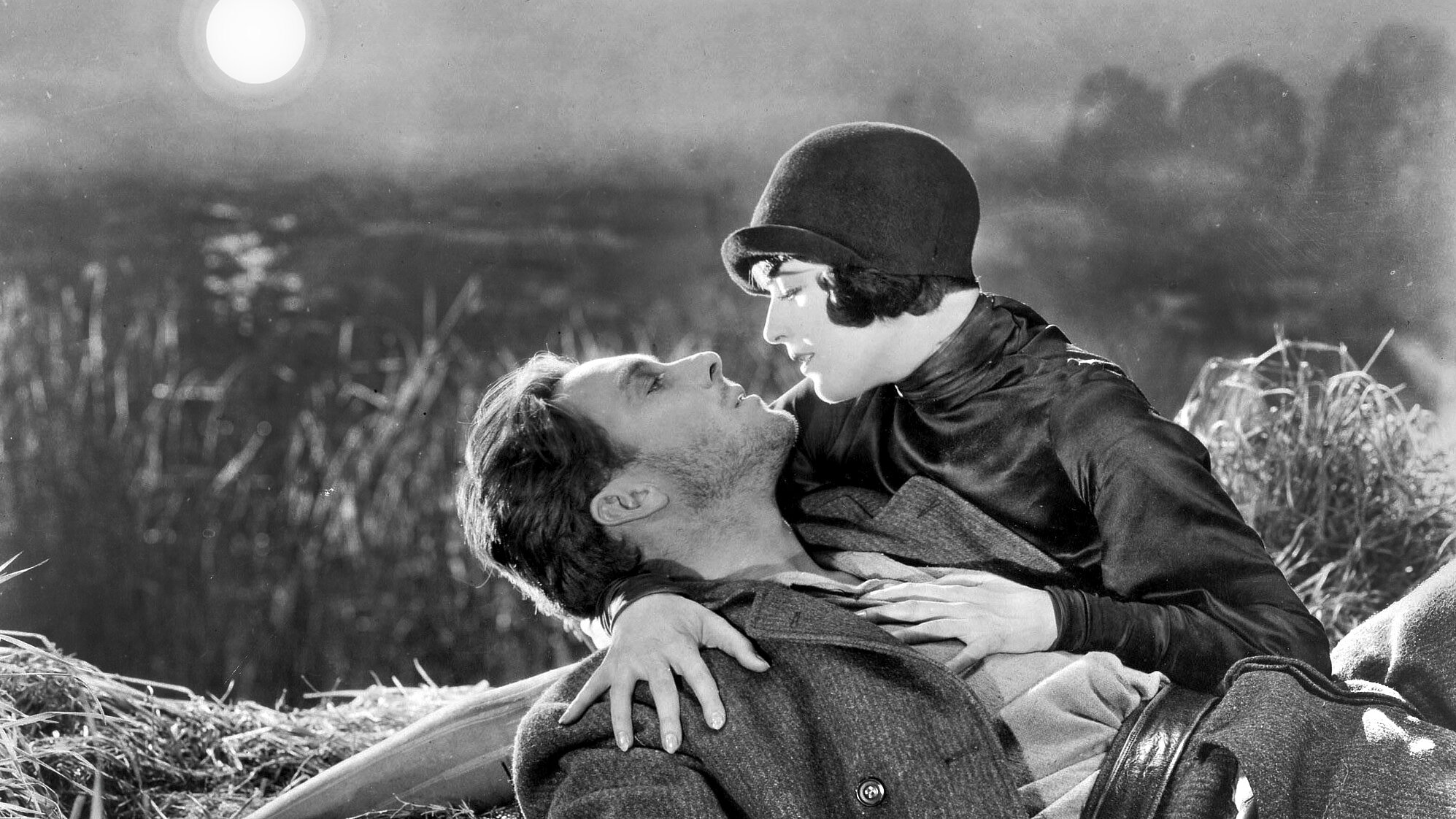 Schwarz-weiß-Filmstill: eine Frau hält einen Mann in einer Landschaft liegend im Arm