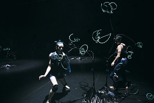 zwei Tänzerinnen bewegen sich in der Nähe eines Gestells mit Magnetspulen