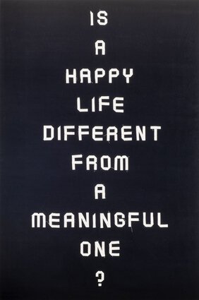 Im Stil eines Plakats ist folgender Satz auf einen auf Keilrahmen aufgezogenen Velourstoff gestickt: Is a happy life different from a meaningful one?