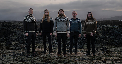 Fünf Personen stehen nebeneinander auf felsigem Boden, alle tragen traditionelle isländische Strickpullover mit Rundkragen und Muster, Gesichter sind unkenntlich gemacht