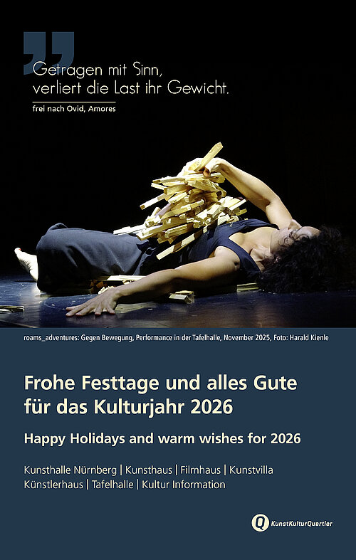 Person liegt auf dem Rücken auf einer Bühne, mit ausgestrecktem Arm und einem Haufen Holzstäben auf dem Oberkörper.