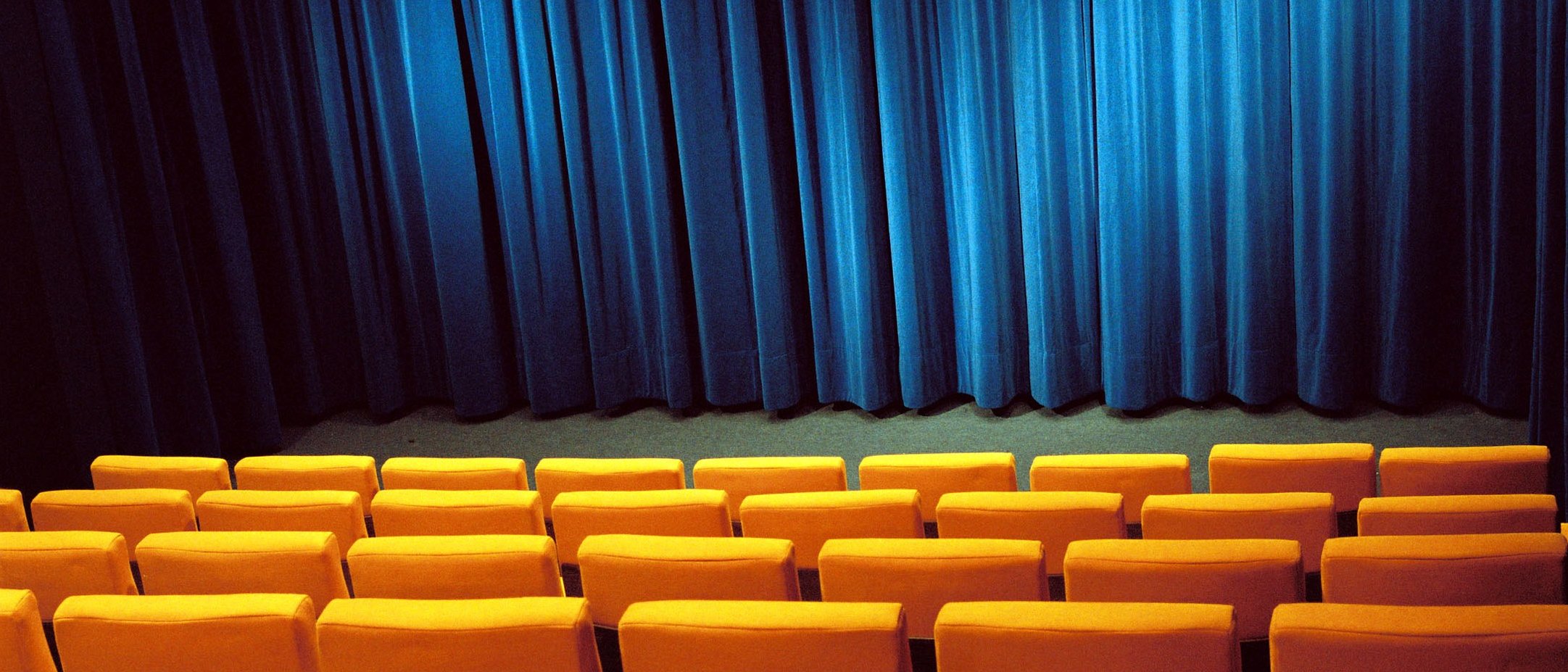 Sitzreihen in einem Kinosaal des Filmhauses mit Blick auf den geschlossenen Vorhang