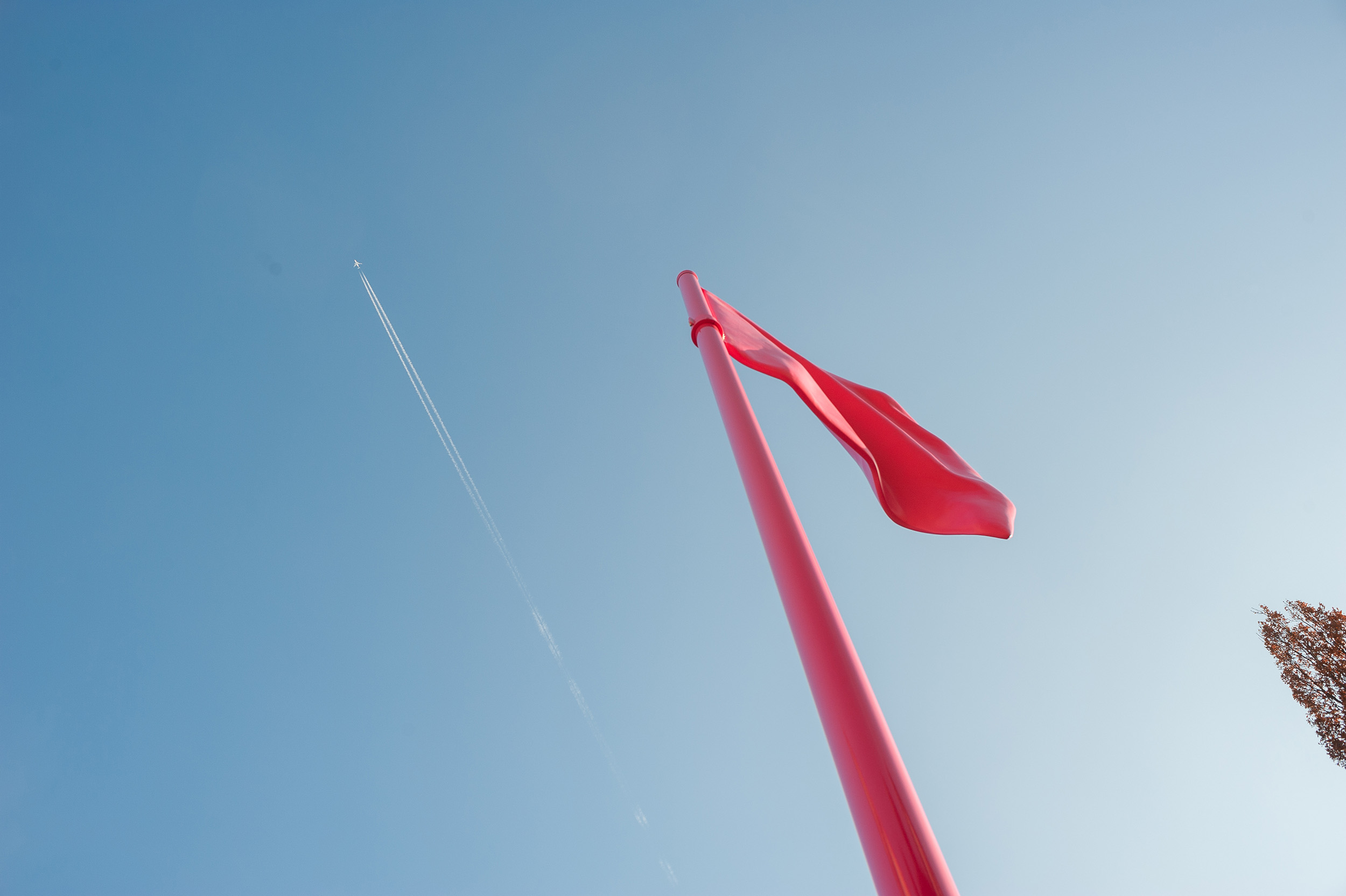 Von unten fotografierte pinke Skulptur der Künstlerin Heidi Sill vor blauem Himmel mit Kondensstreifen eines Flugzeugs