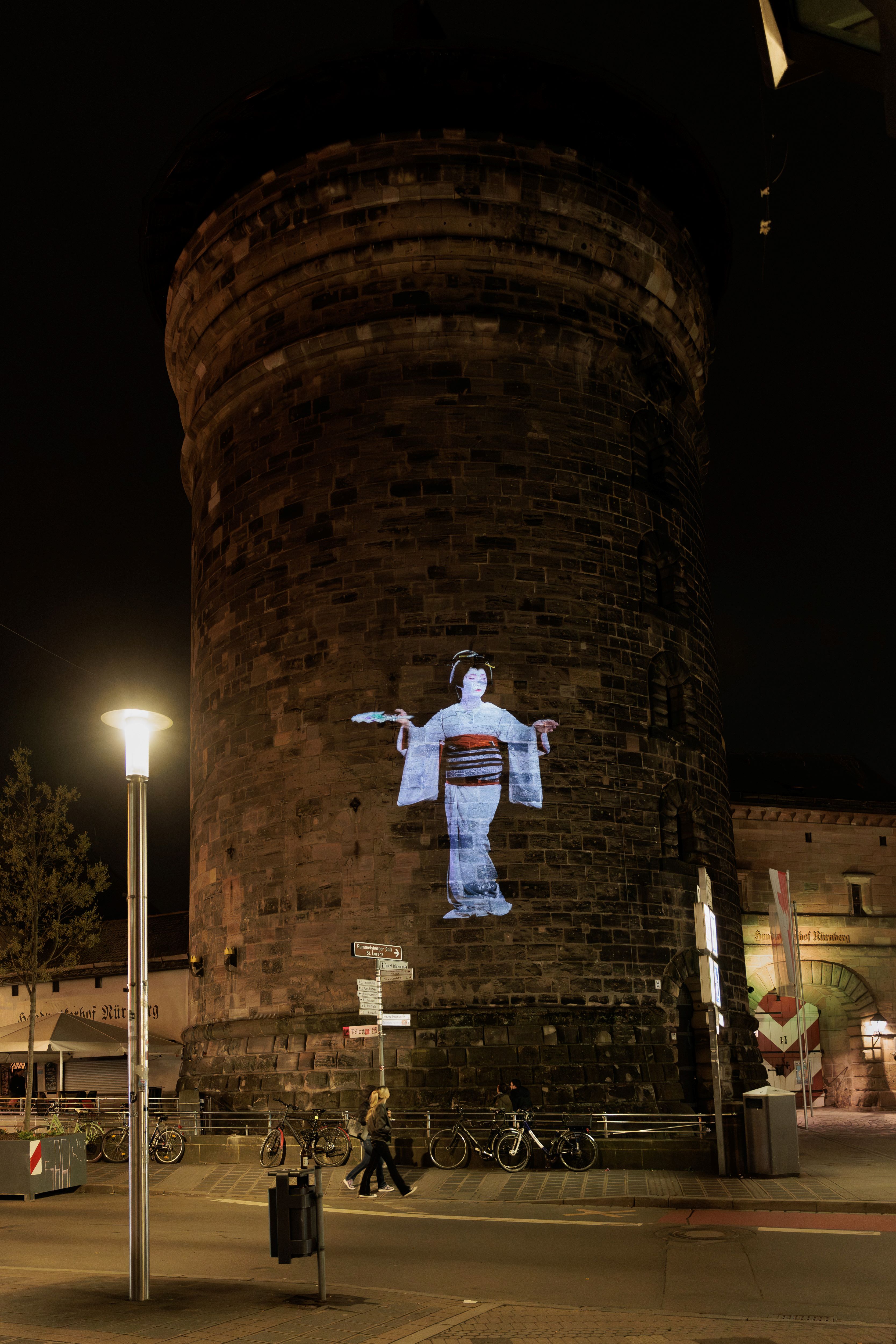 HD-Projektion einer sitzenden Geisha mit traditionellem Kimono auf den runden Backsteinturm Frauentorturm in Nürnberg