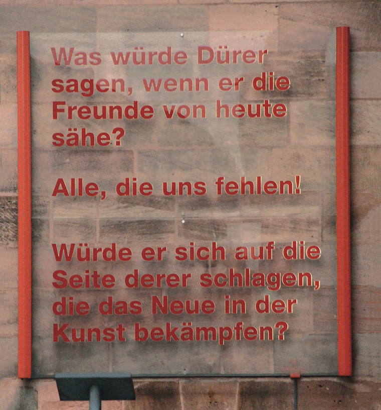 Alt Text: Rote Schrift auf einer grauen Wand mit dem Text 'Was würde Dürer sagen, wenn er die Freunde von heute sähe? Alle, die uns fehlen! Würde er sich auf die Seite derer schlagen, die das Neue in der Kunst bekämpfen?'