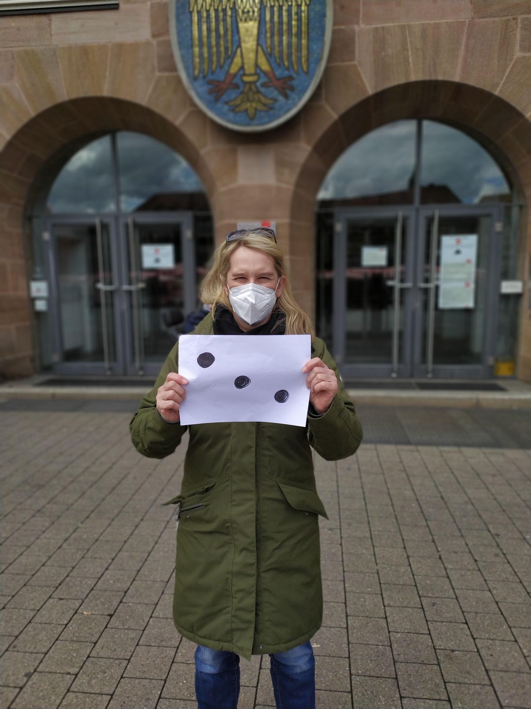 Frau mit Maske vor Rathaus mit Plakat