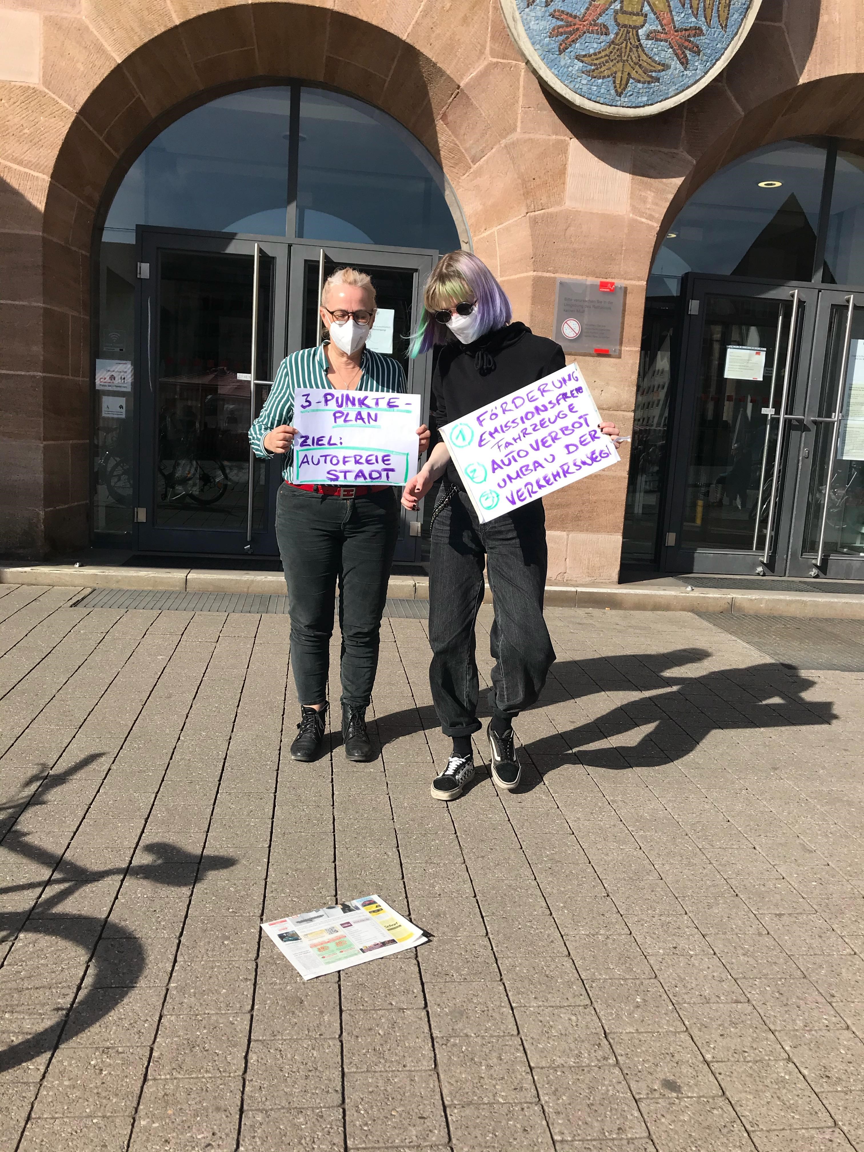 Zwei Personen mit Maske vor Rathaus mit Plakat