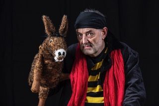 Mann mit schwarzer Kopfbedeckung und rotem Schal neben Plüsch-Esel