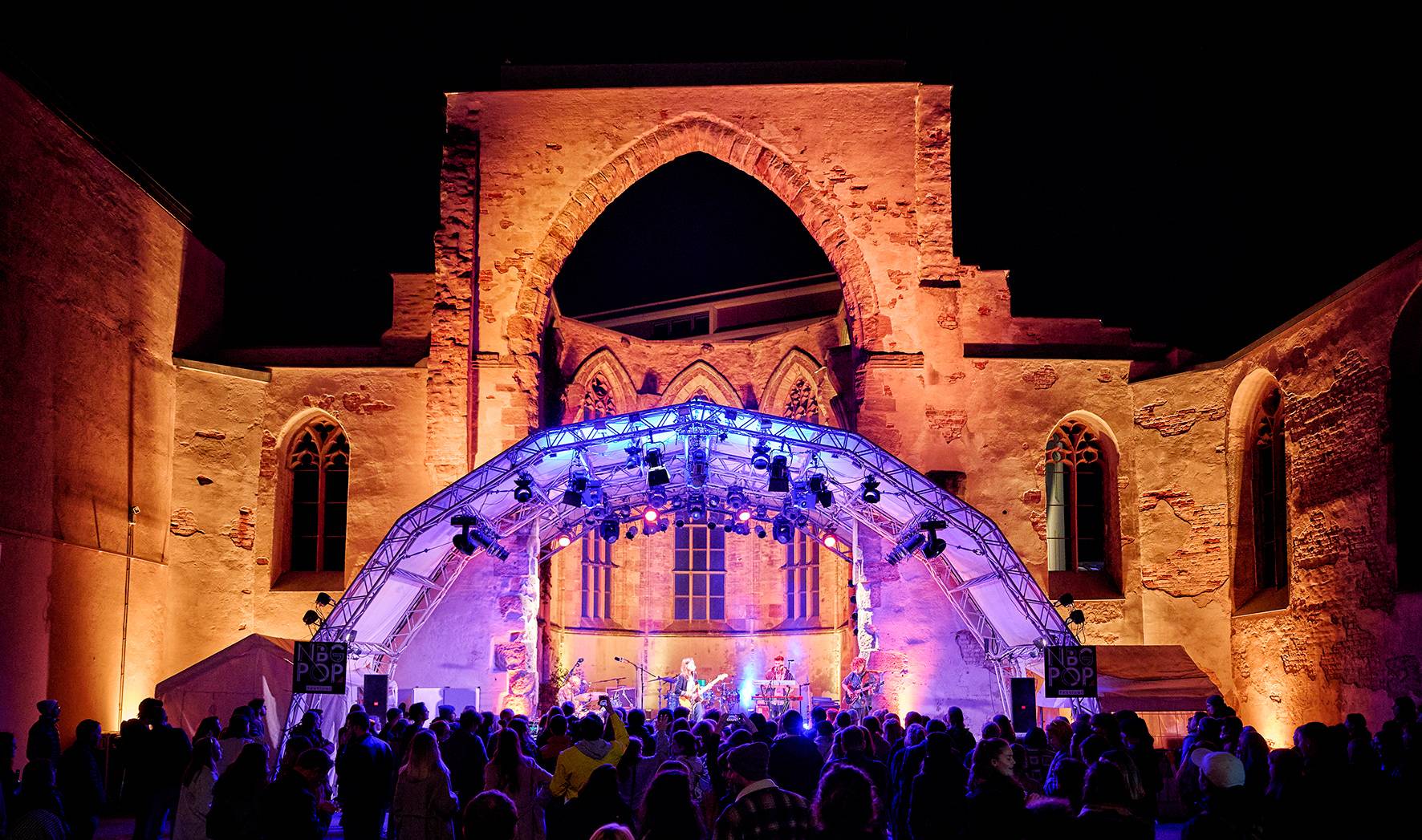 Kirchenruine bei Nacht farbig angeleuchtet mit großer Menschenmenge davor