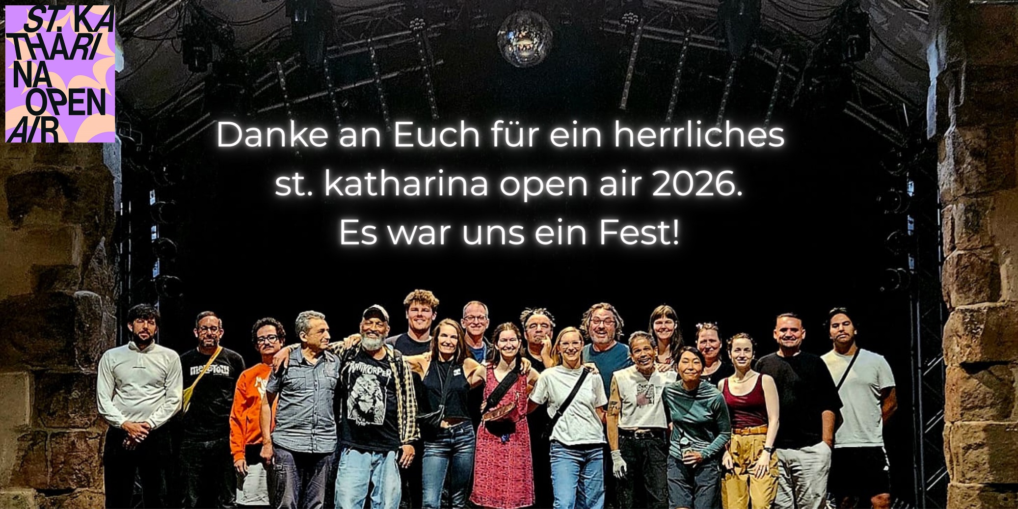 Gruppe von Menschen steht auf einer Bühne unter einer großen Beleuchtungsanlage in einem überdachten Raum