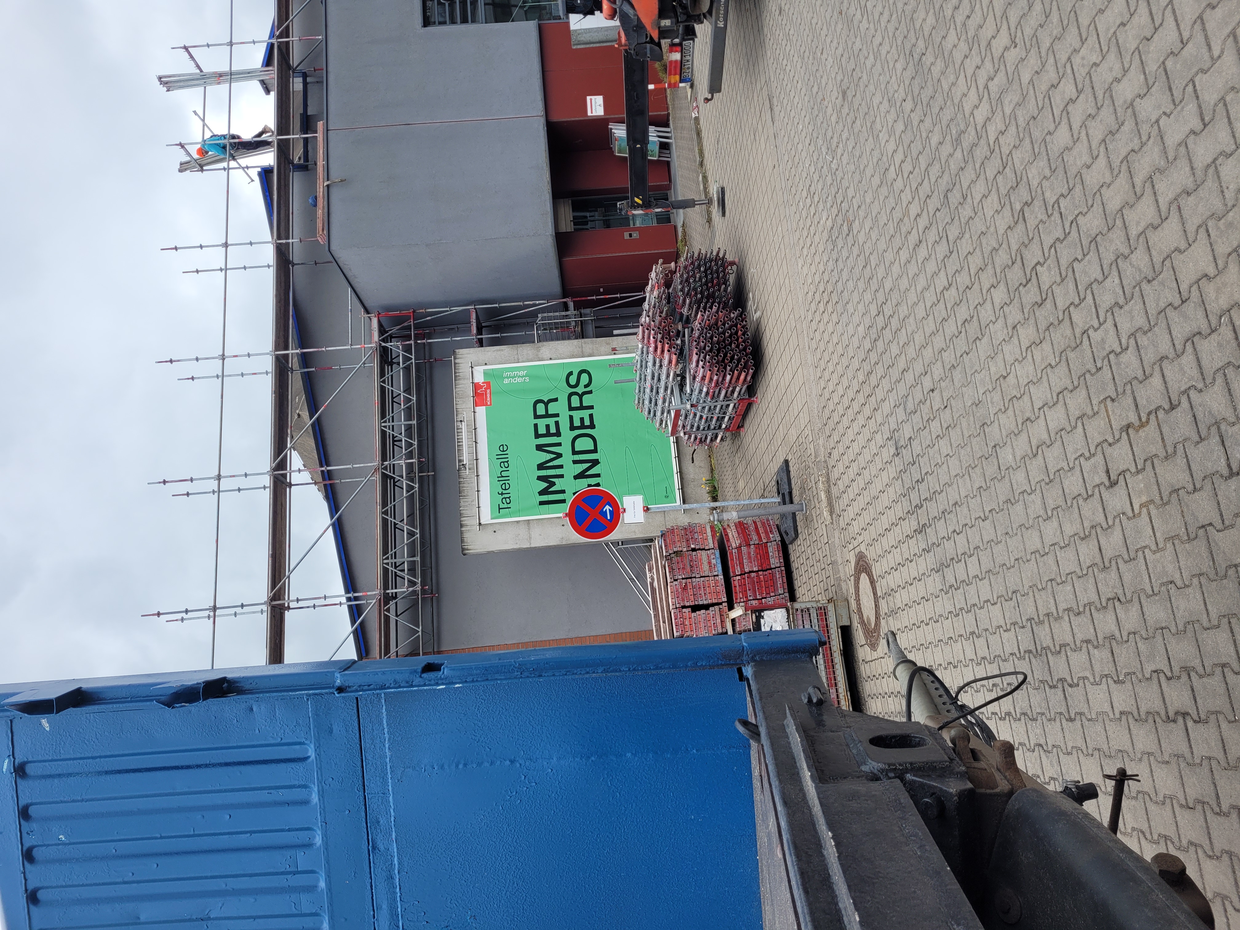 Baugerüst an einem Gebäude mit zwei Arbeitern auf dem Dach und einem Schild mit der Aufschrift 'Tafelhalle IMMER ANDERS'