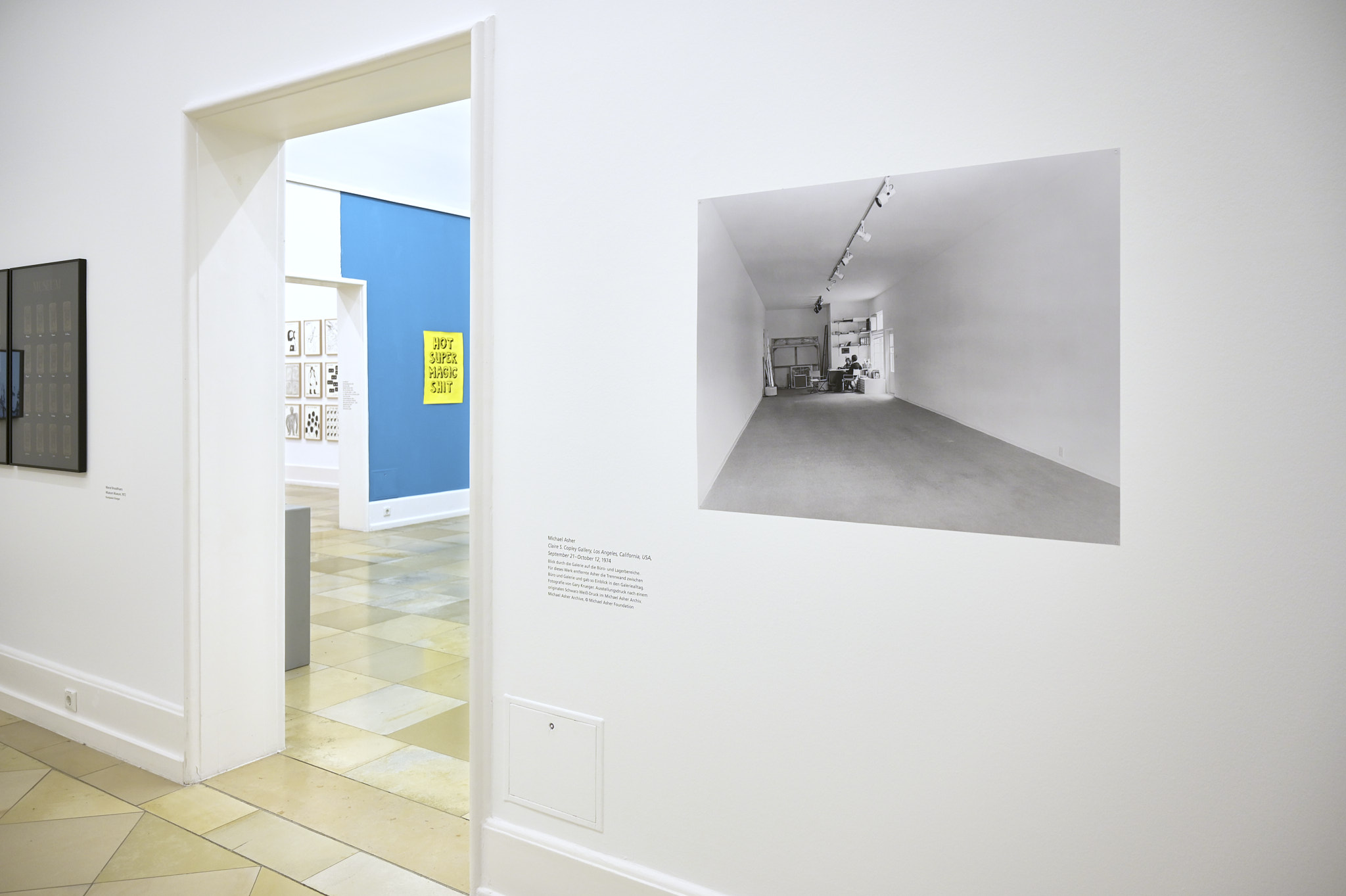 Blick in die Ausstellung mit einem Schwarzweiß-Foto von Michael Asher, das einen leeren Ausstellungsraum in einer Galerie zeigt. Die trennende Wand zum Büroraum der Galerie hat der Künstler entfernt und zum Gegenstand der Ausstellung gemacht.