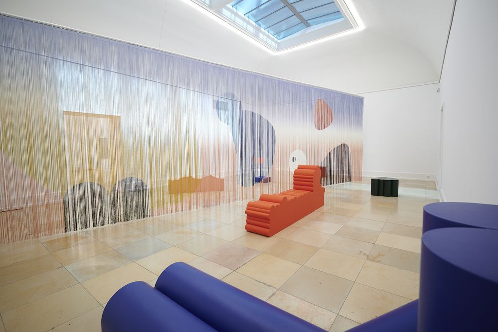 Ein Vorhang aus Fäden quer durch den Raum gespannt, dazu bunte Sitzmöbel aus PU-Schaum