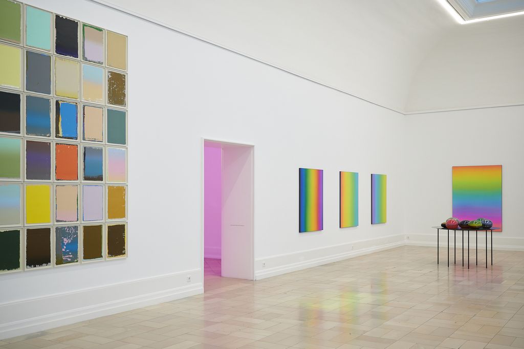 Papierarbeiten in mehreren Schichten übereinander bemalt und als Block gehängt. Seidenbilder in Regenbogenfarben und runde und ellipsoide Glasobjekte.