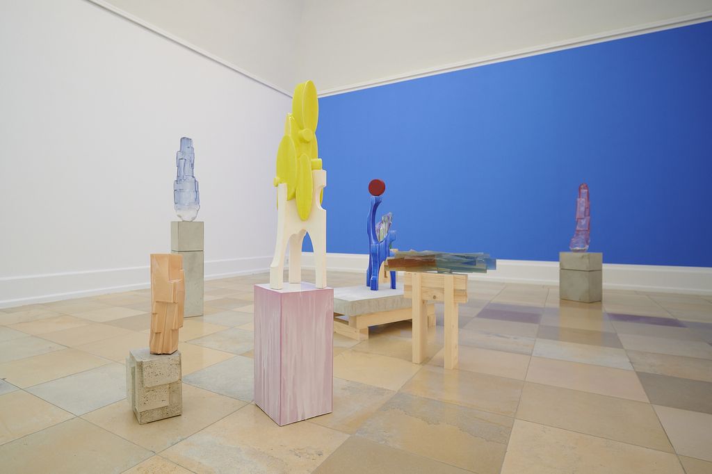 Vor der Wand in der Farbe Himmelblau stehen farbige Glas-, Kunstharz- und Keramikobjekte.