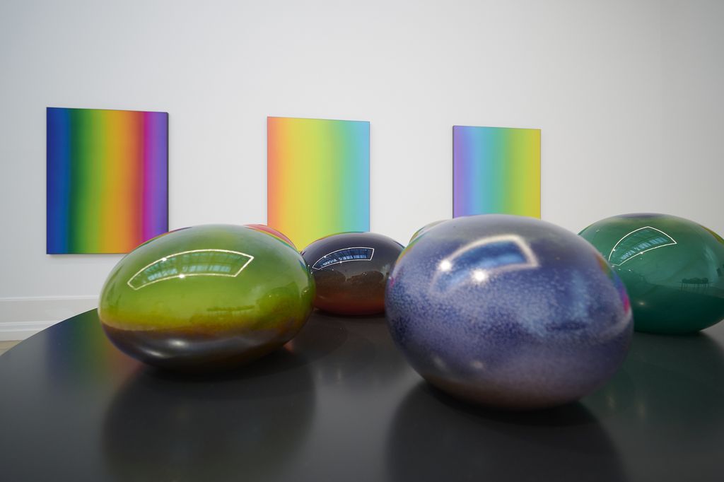 Mundgeblasene runde und ellipsoide Glasobjekte, im Hintergrund Seidenbilder in Regenbogenfarben