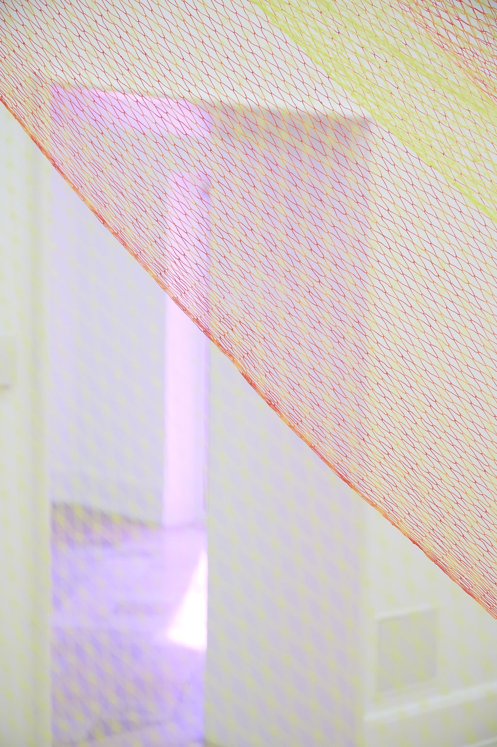 Fischernetze in Neofarben Rot, Orange und Gelb besprüht sind im Raum verspannt