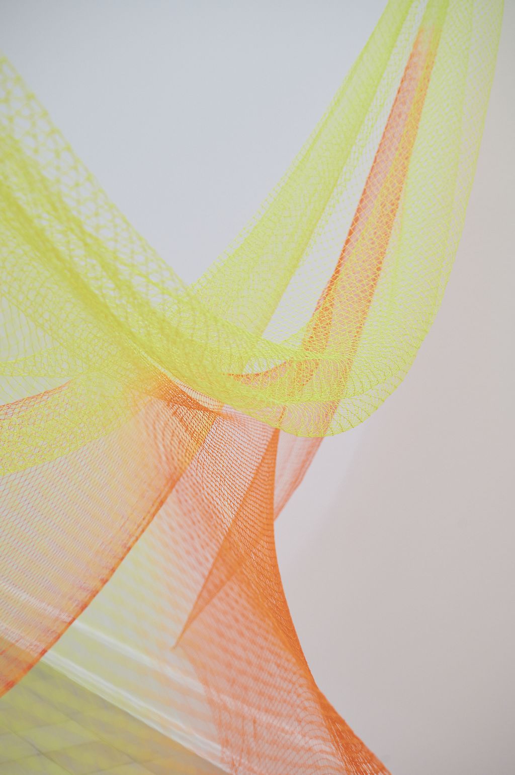 Fischernetze in den Neonfarben Rot, Gelb und Orange sind im Raum verspannt