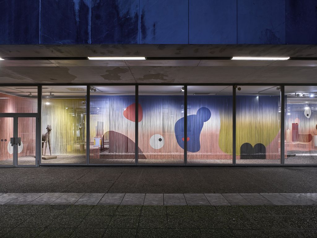 Farbige Fäden von der Decke bis zum Boden hängend bilden in einer Fensterfront eine Gemälde 