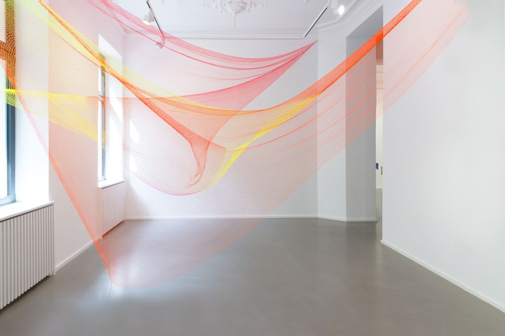 Zwei farbige Fischernetze in Gelb und Orange im Raum verspannt.