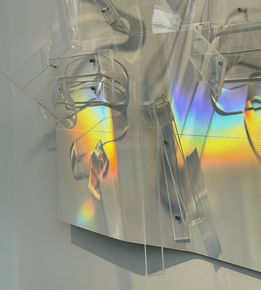 Ein Wandobjekt aus einem Aluminiumlochgitter und Plexiglasteilen, das mit der Bewegung der Betrachtenden stellenweise in verschiedenen Neonfarben leuchtet.