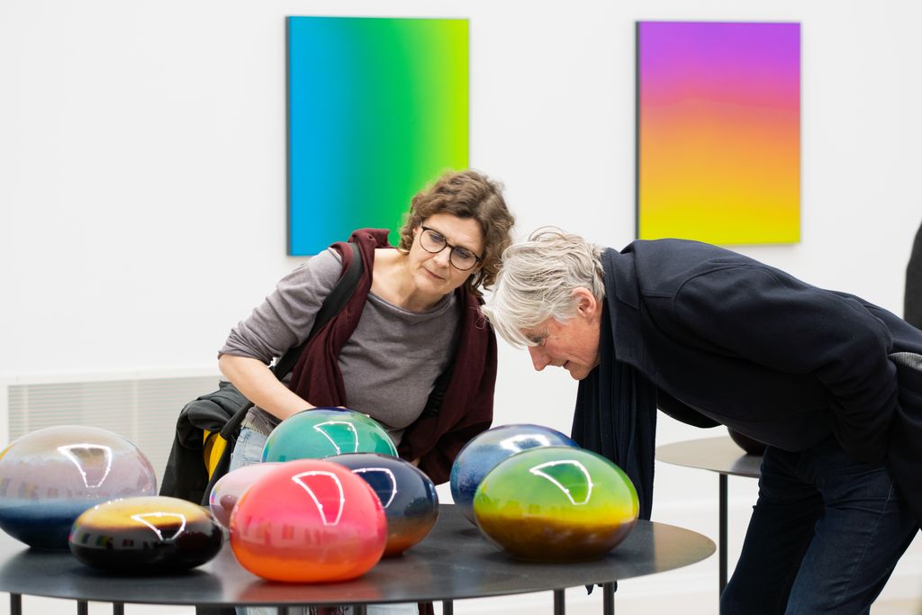 Gemälde in regenbogenfarbiger Seidenmalerei, davor bunte, mundgeblasene Glaskörper von Matti Braun