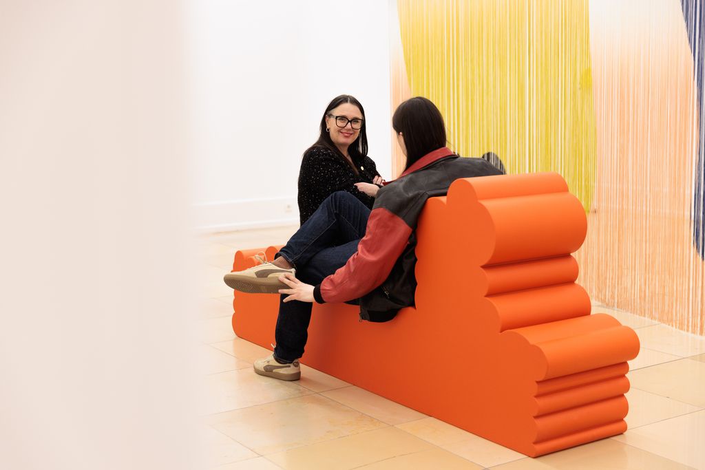 rotes Sitzmöbel vor farbigen Fadenvorhang von Erika Hock