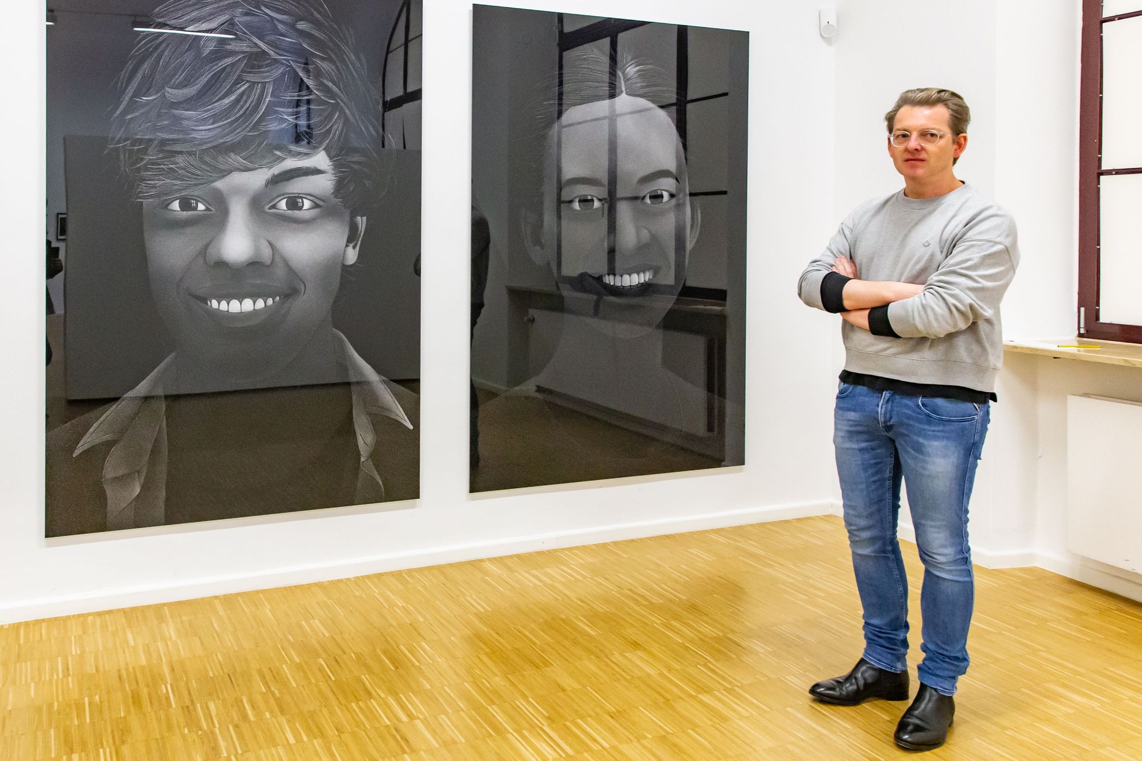 Der Künstler Thilo Westermann vor seinen beiden großformatigen Porträts von Jugendlichen, die Selbstmord begingen, weil sie diskriminiert wurden und mit ihrer ihnen biologisch zugewiesenen Identität nicht weiterleben konnten