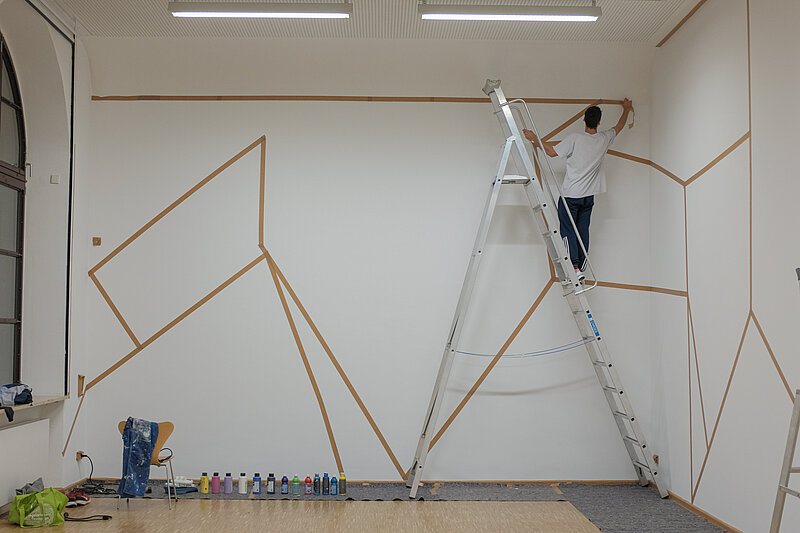 Ein Mensch steht auf einer Leiter und beklebt eine Wand