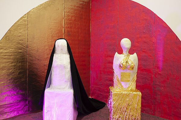 2 Skulpturen stehen nebeneinander vor goldenem und rotem Hintergrund